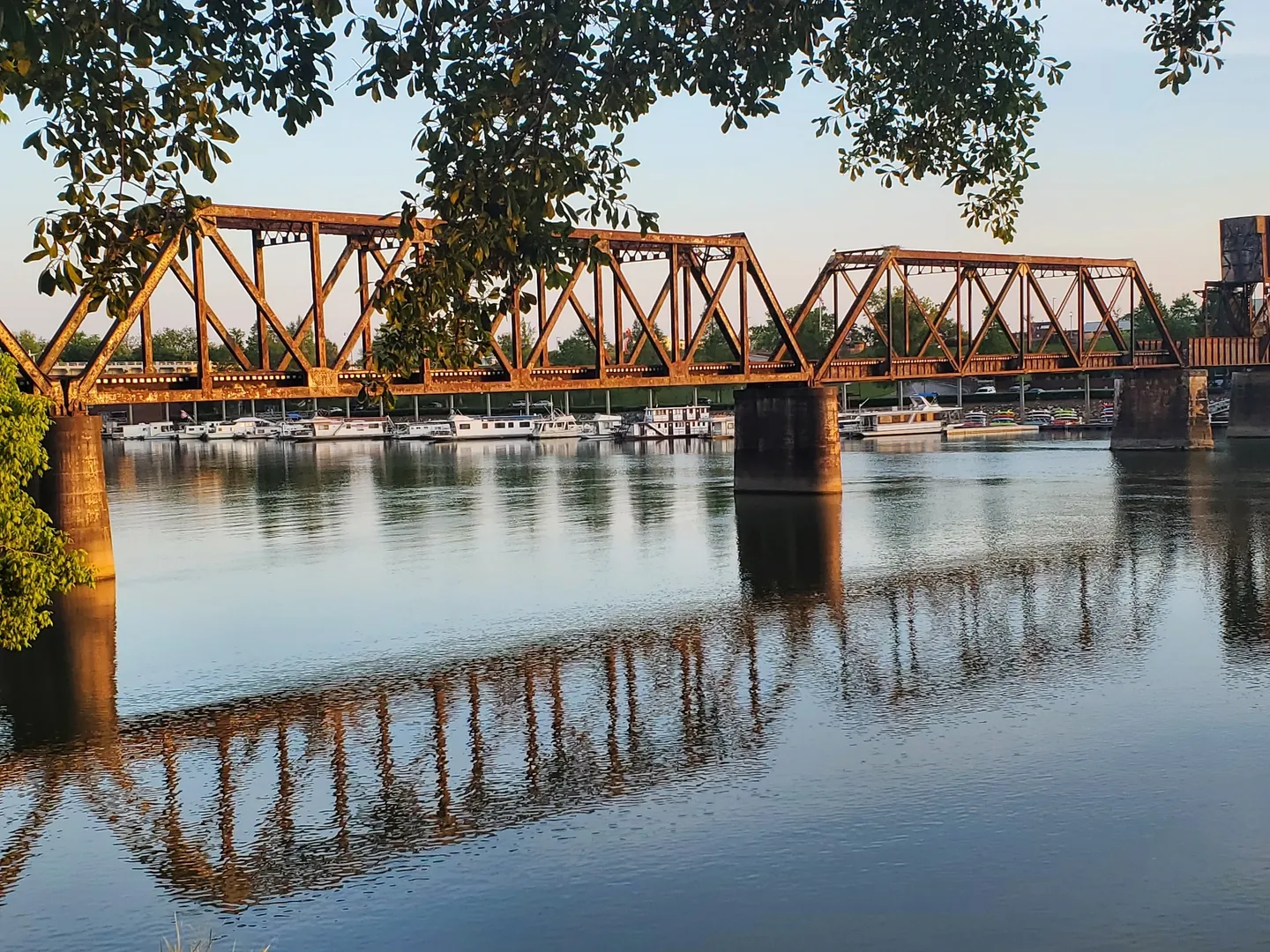 A train bridge over a river with boats on it.